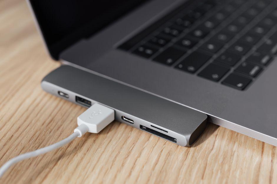 Un adaptateur multiport relié par un câble blanc à un ordinateur portable posé sur un bureau en bois