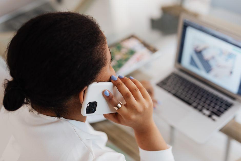 Une femme au téléphone à son bureau, devant un ordinateur portable ouvert