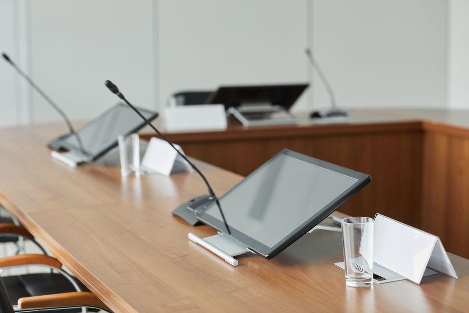 Microphones de table et tablettes posés sur une longue table en bois, dans une salle de réunion lumineuse