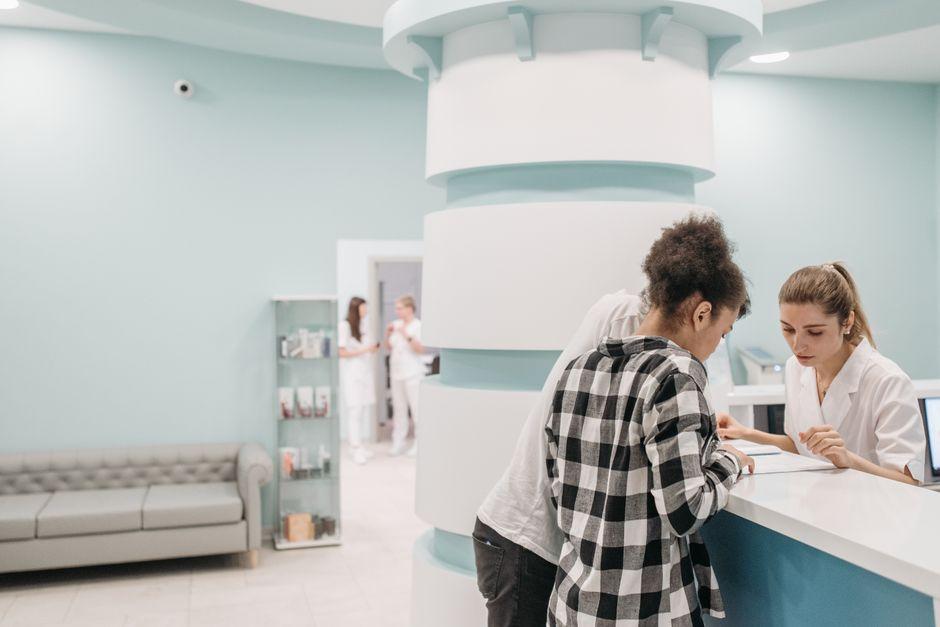 Eine Patientin und eine Mitarbeiterin am Empfangstresen einer hellen Arztpraxis