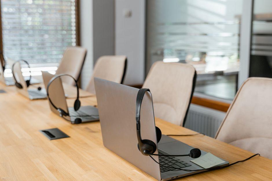 Headsets resting on laptops along a long wooden table, with empty chairs behind