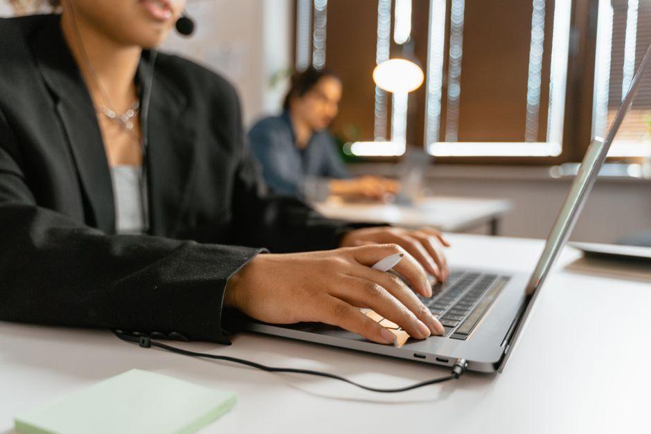 Une conseillère de service client, casque-micro sur la tête, tape sur un ordinateur portable dans un bureau lumineux