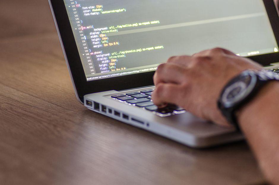 A hand typing on a laptop whose screen shows lines of code
